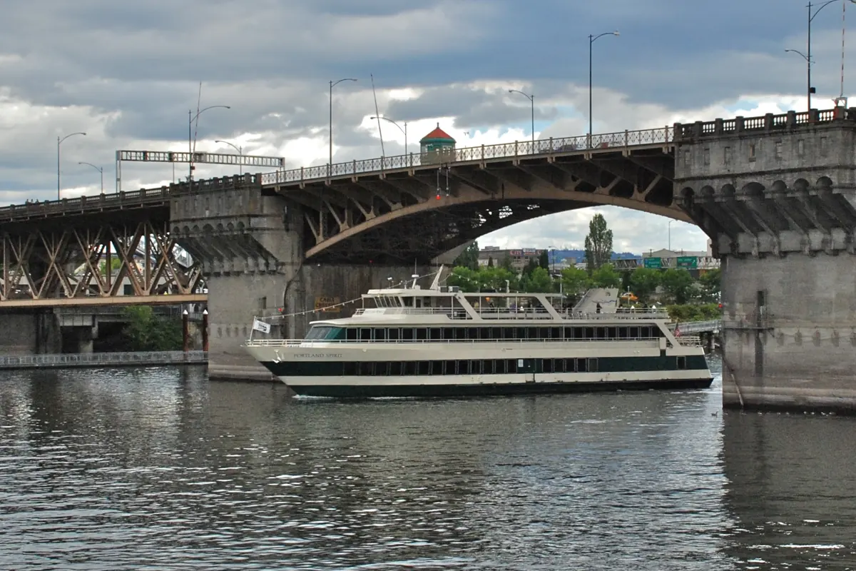 A Portland Spirit Cruises boat passing under the arched concrete and steel spans of the Burnside Bridge