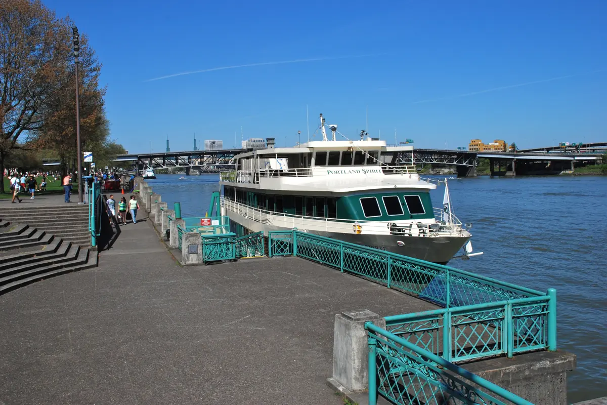 The Waterfront Park dock in downtown Portland, with concrete steps, a teal railing and a cruise boat moored alongside