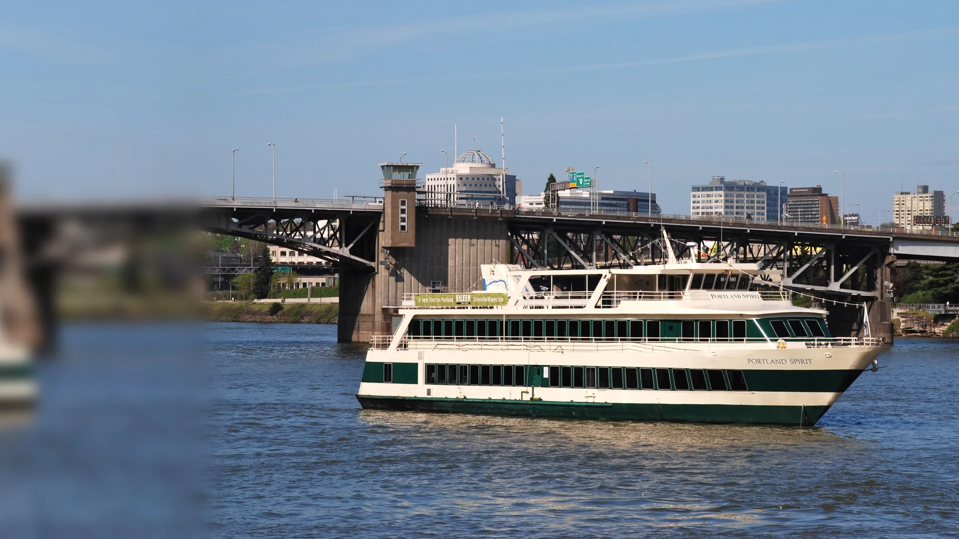 A cream-and-green Portland Spirit dinner boat on the Willamette River below the Morrison Bridge in downtown Portland
